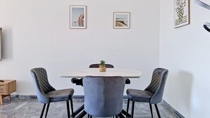 Et spiseområde med et hvidt bord, fire grå polstrede stole og to billeder i rammer på væggen.