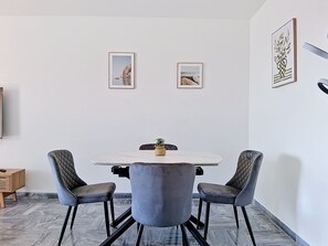 Ein Essbereich mit einem weißen Tisch, vier grau gepolsterten Stühlen und zwei gerahmten Bildern an der Wand.