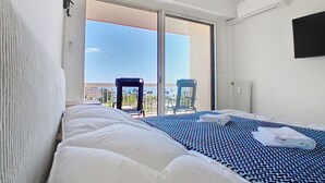 Et hotelværelse med en seng, en stol, et fjernsyn og en balkon med udsigt.
