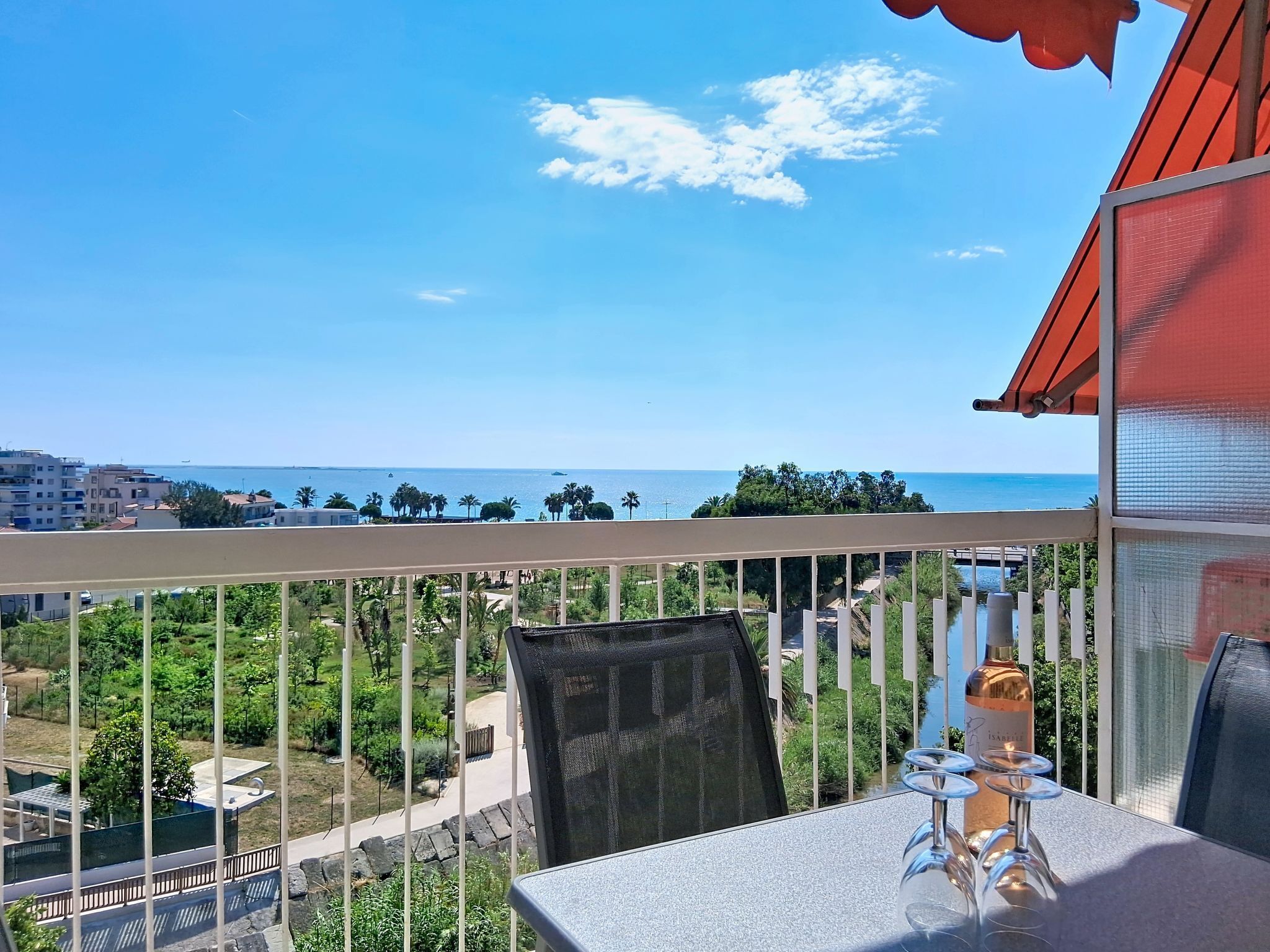 A balcony with a view of the sea, a table with a bottle and glasses, and a chair.