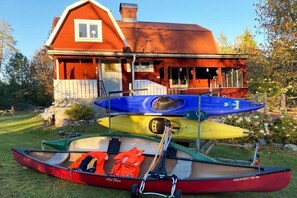 A red house with a porch, a red canoe, and a blue and yellow canoe in front. - Holiday home in Smaland with 4 bedrooms (Kvillsfors)