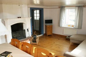 A room with a fireplace, a television on a wooden cabinet, a sofa, and a window with curtains. - Holiday home in Smaland with 4 bedrooms (Kvillsfors)