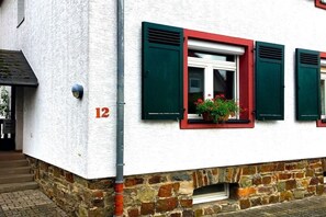 Ein Gebäude mit weißer Fassade, Hausnummer 12 und grünen Fensterläden.