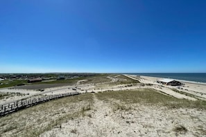 Eine Küstenlandschaft mit sandigem Strand, einem hölzernen Steg und einem Gebäude mit flachem Dach.