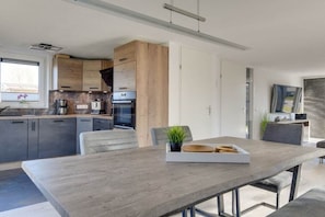 Eine moderne Küche mit eingebauten Geräten, ein Essbereich mit Holztisch und Blick ins Freie.