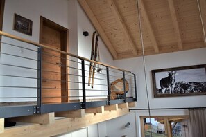 Ein Loft-Zimmer mit Holzbalkendecke, einer erhöhten Zwischenebene mit Metallgeländer und einem gerahmten Bild eines Elchs.