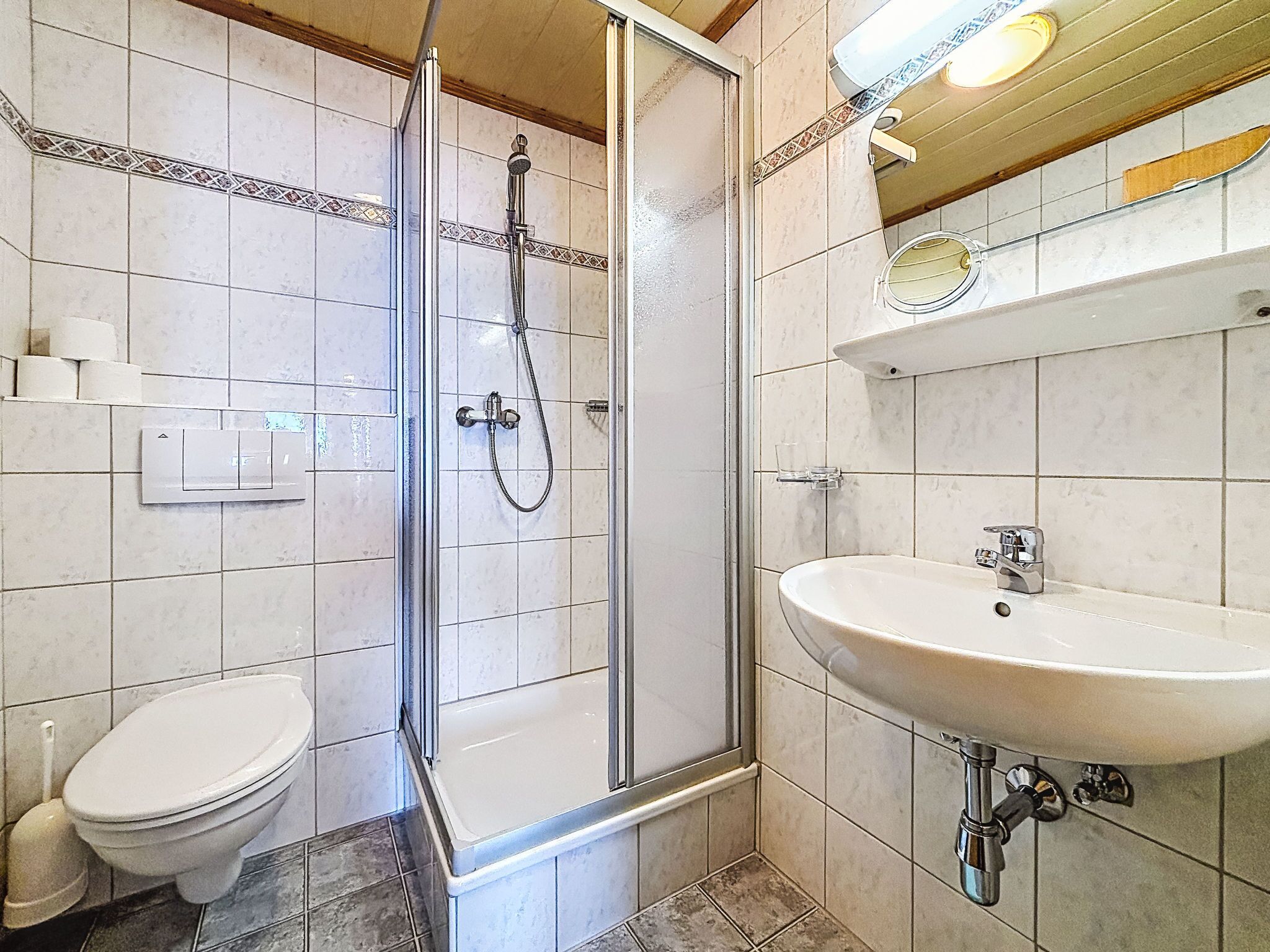 Une salle de bain avec une douche à parois de verre, des toilettes blanches et un lavabo avec un miroir au-dessus.