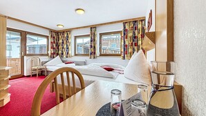 A hotel room with a bed, a desk, a chair, a table, and a view of the city through large windows. - Wiesenhof by Interhome (Kappl)
