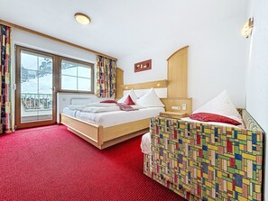 Habitació d'hotel amb un llit, una petita taula de nit, una cadira, una finestra amb cortines i vista a un paisatge nevado.