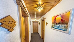A hallway with wooden doors, a number sign, a painting, and a ceiling light fixture. - Wiesenhof by Interhome (Kappl)