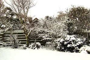 A snow-covered garden with a wooden fence, leafless trees, and a house in the background. - Holiday apartment with 1 bedroom (Callantsoog)