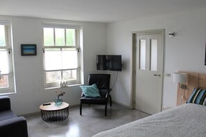 Ein Zimmer mit einem Bett, einem Sessel, einem Fernseher und einem Fenster.