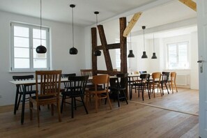 A dining area with wooden chairs and tables, black pendant lights, and exposed wooden beams. - The yellow holiday home (Irmenach)