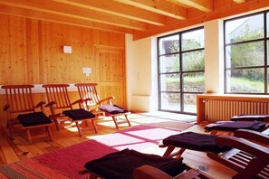 A room with wooden walls and large windows, wooden chairs, and a red rug. - The yellow holiday home (Irmenach)
