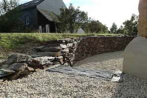 A stone wall, gravel path, and a house with a sloped roof. - The yellow holiday home (Irmenach)