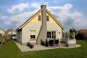 Ein zweistöckiges Haus mit Ziegelaußenwand, gelbem Zierstreifen und einem Schornstein.