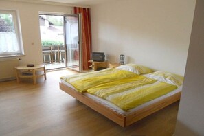 Ein Schlafzimmer mit Bett, Fernseher, einem kleinen Tisch und einer Schiebeglastür, die zu einem Außenbereich führt.