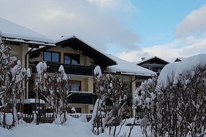 Ein mehrstöckiges Gebäude mit Balkonen, umgeben von schneebedeckten Bäumen und einem klaren Himmel.