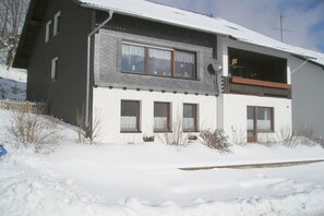 A two-story building with a balcony, a chimney, and a snow-covered ground. - Holiday home with 8 bedrooms (Medebach-Düdinghausen)