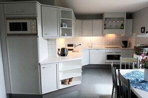 Eine kompakte Küche mit weißen Schränken, einer Mikrowelle, einer Kaffeemaschine und einem Essbereich mit Tisch und Stühlen.