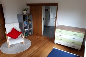 Ein Zimmer mit einem weißen Stuhl, einem roten Kissen, einem Bücherregal, einem Holzschrank und einer Küchenzeile.