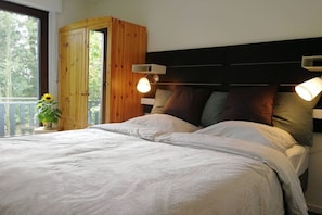 A bedroom with a bed, wooden wardrobe, bedside lamps, and a view of trees. - Sauerlandhaus Küstille (Medebach)