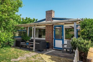 A covered outdoor seating area with a table and chairs, a brick chimney, and a blue door. - Holiday home with 2 bedrooms (Callantsoog)