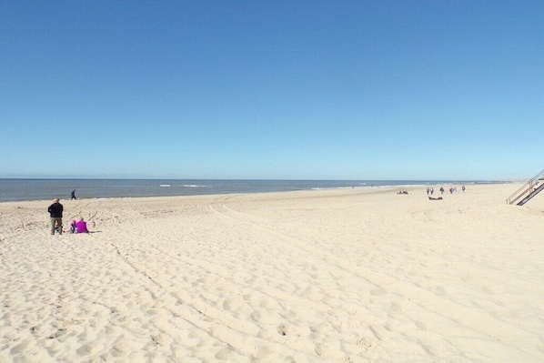 A wide sandy beach with a clear sky, a few people, and a staircase leading down to the water. - Holiday home with 2 bedrooms (Callantsoog)