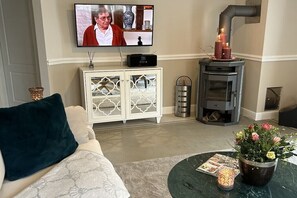 Ein Wohnzimmer mit einer Couch, einem Fernseher, einem Kamin, einer Kommode und einem Couchtisch mit Blumen.