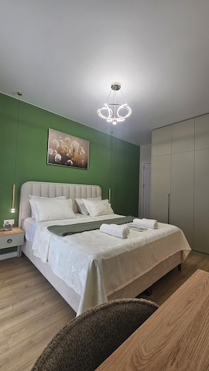 A modern bedroom with a bed, green walls, a pendant light, a painting, and a wardrobe. - Cozy 1-bedroom apartment in enchanting T'bilisi with (T'bilisi)