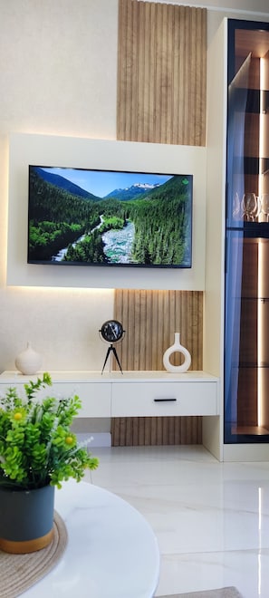 A modern living room with a flat-screen TV mounted on the wall, a white console table with a vase and clock, and a potted plant on a round table. - Cozy 1-bedroom apartment in enchanting T'bilisi with (T'bilisi)
