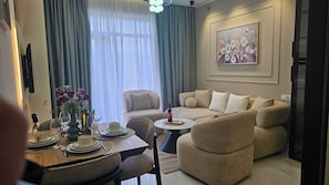 A living room with a sofa, a dining table set with plates, glasses, and a bottle, and a painting on the wall. - Cozy 1-bedroom apartment in enchanting T'bilisi with (T'bilisi)