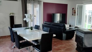 Et spiseområde med et hvidt bord og sorte stole, en sort sofa, et fjernsyn og en pejs.