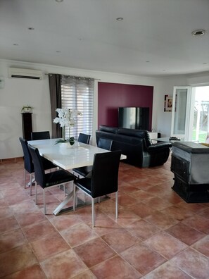 A dining area with a white table and black chairs, a black sofa, a TV, and a fireplace. - Beautiful, quiet, air-conditioned villa with swimming pool (Poulx)