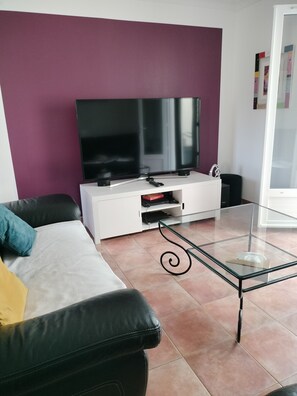 A living room with a flat-screen TV, a white entertainment unit, a glass coffee table, and a black leather sofa. - Beautiful, quiet, air-conditioned villa with swimming pool (Poulx)
