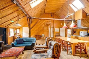 Ein geräumiges Dachzimmer mit einer hohen Holzbalkendecke, einem Esstisch und einem blauen Ledersofa.