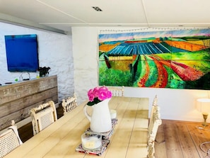 A dining area with a wooden table, chairs, a vase of flowers, a candle, and a large colorful painting on the wall. - House - Sleeps 6 - Pet Friendly - Parking (Castle Douglas)