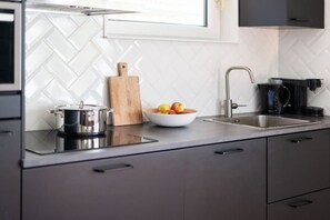 Eine moderne Küche mit Kochfeld, Schneidebrett, Obstschüssel, Spüle und Kaffeemaschine.