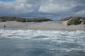 Ein Strand mit Wellen, Dünen und einer Person, die im Sand steht.