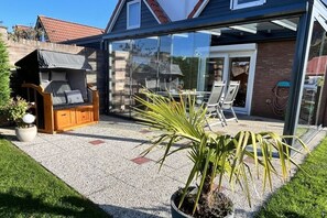 Ein modernes Haus mit einer gläsernen Veranda, Sitzgelegenheiten im Freien und einem Blumentopf.