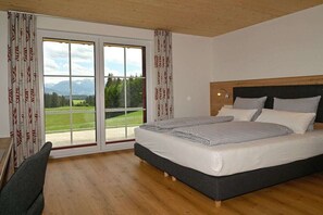 Une chambre avec un grand lit, un bureau et une vue sur les montagnes, visible à travers une porte coulissante.