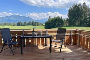 Une terrasse en bois avec deux chaises et une table, offrant une vue sur un paysage montagneux.