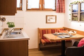 Eine kleine Küchenzeile mit Spüle, ein Fenster mit Vorhängen, ein gerahmtes Bild an der Wand und eine Sitzbank in der Ecke.