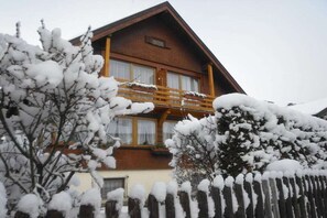 Eine zweistöckige Chalet mit Holzbalkon, umgeben von schneegebundenen Bäumen.