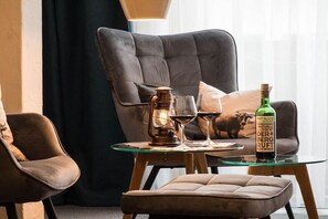 Ein gemütlicher Sitzbereich mit gepolstertem Sessel, Hocker und einem Glastisch mit Flasche und Gläsern.