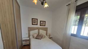 Un dormitorio con cama, mesitas de noche, armario y ventana con cortinas.