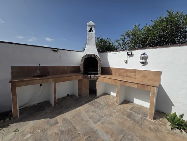 An outdoor kitchen with a stone countertop, a sink, and a chimney. - Cuervi house with private pool in Conil. (Conil De La Frontera)