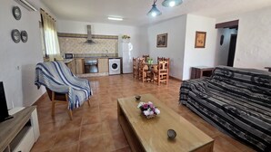 Una sala de estar con sofá, una mesa de centro, un mueble para televisión, un comedor con sillas y una mesa, y una cocina con lavadora y refrigerador.