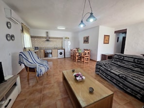 A living room with a sofa, a coffee table, a TV stand, a dining area with chairs and a table, and a kitchen with a washing machine and a refrigerator. - Cuervi house with private pool in Conil. (Conil De La Frontera)