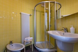 Ein Badezimmer mit gelben Fliesen, einer Duschkabine, einem Waschbecken und einem Bidet.
